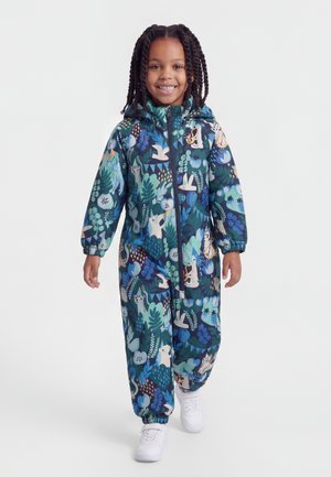 Naeratav laps kõnnib edasi, kandes kapuutsiga kombinesooni sinise ja rohelise abstraktsete loomade ja taimede mustritega ning valgeid tossusid.