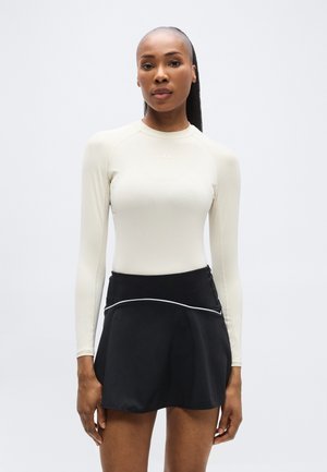 Pikad varrukad hele beež top, mis on ühendatud musta seelikuga, millel on kontrastne valge ääris ja lõdvestatud disain. Sile kangapind.