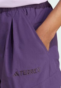 Purple Terrex shorts with an elastic waistband, side pockets, and embroidered logo detail. Made of textured, lightweight fabric.