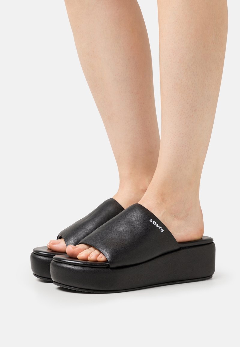 Sandales à plateforme noires avec une tige en cuir lisse et un design à bout ouvert, présentant un talon surélevé et un détail de logo blanc.