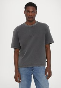Grå bomulds t-shirt med rund hals, korte ærmer og et diskret logo på brystet. Løs pasform og synlige syninger.
