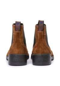 Bottines en daim marron avec des panneaux élastiques noirs, des languettes texturées au talon et une semelle en caoutchouc noir striée ; design épuré et minimaliste.