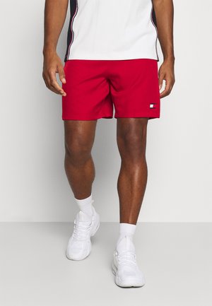 Røde badeshorts med et lille logo på den nederste kant, kombineret med hvide træningssko og sokker. Glat tekstur, midt på låret i længden.