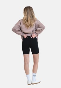 Černé šortky, oversize béžová mikina, bílé ponožky s černým textem a bílé tenisky. Dlouhé, vlnité vlasy padající dolů po zádech.