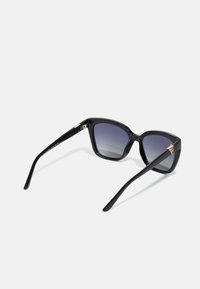 Black plastic sunglasses with a structured cat-eye shape, gradient dark gray lenses, and gold-tone accents on the temples.