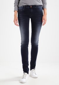 Úzké džíny z tmavě modrého denimu s vybledlým předním dílem, klasickým pětikapsovým designem a zapínáním na jeden knoflík. Kombinovány s bílými teniskami.