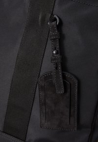 Czarny plecak z tkaniny z teksturowanym, zamszowym detalem oraz solidnym paskiem. Charakteryzuje się gładkim, matowym wykończeniem oraz kontrastowym ściegem.