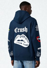 Sweat à capuche bleu marine en mélange de coton, avec un grand graphisme de lèvres blanches, le mot "Crush" et divers détails imprimés sur les manches.