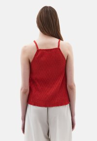 Top in maglia rossa con spalline regolabili, superficie texturizzata e orlo leggermente svasato. La vista posteriore mostra il posizionamento delle spalline e la vestibilità.