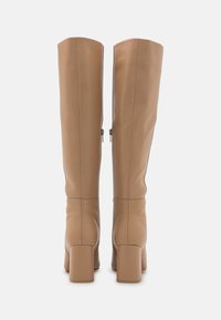 Paire de bottes hautes en cuir fauve avec talons carrés, vue de dos, sur un fond blanc uni.