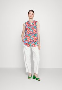 Top sem mangas floral com padrões em vermelho, azul, verde e branco, combinado com calças brancas e sandálias de salto verdes.