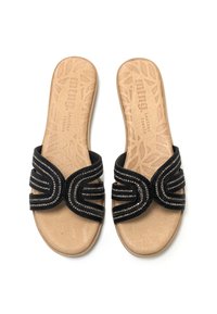 Chanclas negras con múltiples bandas retorcidas que presentan acentos metálicos, plantilla de cuero beige con un patrón de hojas y suela plana.
