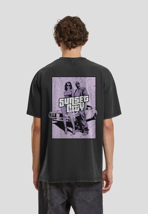 Mann trägt schwarzes T-Shirt mit lila Grafik von einem Mann und einer Frau, die vor einem Auto stehen, und dem Text "Sunset City Life" auf dem Rücken.