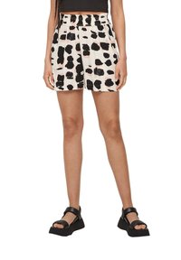 Woman wearing black strap sandals and high-waisted shorts with black and pale pink irregular spots on white background.