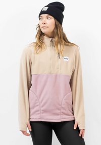 Fleece pullover met een halve rits, voorzien van een lichtbeige bovenkant en roze onderkant. Inclusief zijzakken en een merklabel op de borst. Zwarte beanie gedragen.