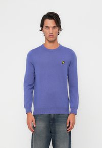 Lila Pullover mit langen Ärmeln, rundem Ausschnitt und einem kleinen gelben Schmetterlingslogo auf der Brust. Weicher Stoff und figurnahes Design.