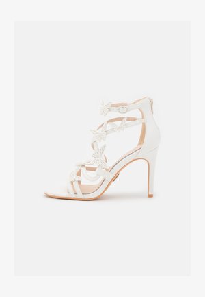 White high-heeled sandal with butterfly accents, open toe design, adjustable ankle strap, and smooth synthetic material.