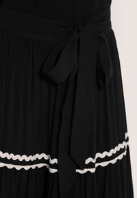 Schwarzes Kleid mit gebundenem Taillengürtel, plissierter Textur und kontrastierendem weißen Wellenrand am Saum. Weicher Stoff, fließendes Design.