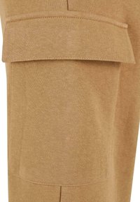 Beige Cargo-Hosen mit einer großen Klappen-Tasche am Oberschenkel, aus einem weichen, strukturierten Stoff mit sauberer Naht und einer taillierten Passform.