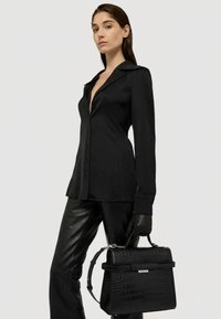 Svart långärmad skjorta med krage, i kombination med svarta läderbyxor. Håller en strukturerad svart handväska med krokodilprägling.