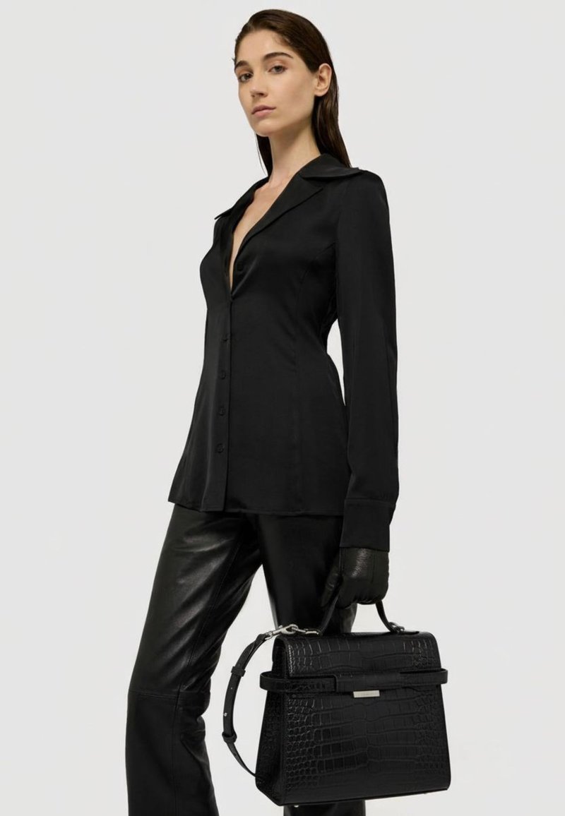 Svart långärmad skjorta med krage, i kombination med svarta läderbyxor. Håller en strukturerad svart handväska med krokodilprägling.