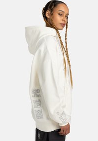 White hoodie made of soft fabric, featuring a large hood, side seams, and graphic text on the sleeves. The design is relaxed fit.