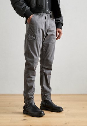 Gray cargo pants with elastic cuffs and side pockets, paired with sleek black ankle boots featuring a buckle detail and textured soles.