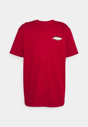 T-shirt en coton rouge avec un col rond, des manches courtes et un petit design brodé sur la poitrine, comprenant des éléments verts et blancs.