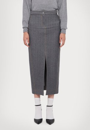 Kobieta ubrana w szarą spódnicę midi w prążki z rozcięciem z przodu, szary sweter, białe skarpetki oraz czarne szpilki z paskiem wokół kostki.