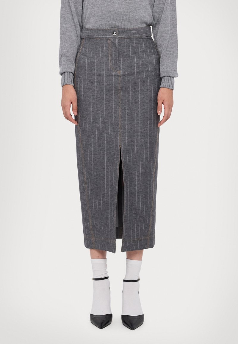 Femme portant une jupe midi grise à fines rayures avec une fente à l'avant, un pull gris, des chaussettes blanches et des talons noirs à bout pointu avec des lanières à la cheville.