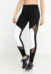 Leggings en blanco y negro con acentos de panel de malla, cintura alta, material elástico y patrón geométrico, diseñados para ropa de actividad.