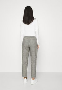 Grå rutiga byxor med avslappnad passform, elastisk midja och två bakfickor, ihop med vita sneakers.