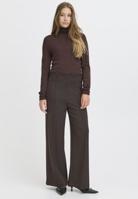Bela turtleneck jopica v kombinaciji s svetlo rjavimi hlačami širokega kroja, ki imajo vzorec houndstooth. Črne čevlje s konico zaključujejo obleko.