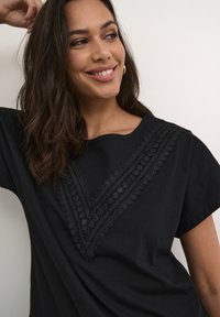 T-shirt en coton noir avec une bordure en dentelle décorative en forme de V au niveau du col. Manches courtes et texture lisse.