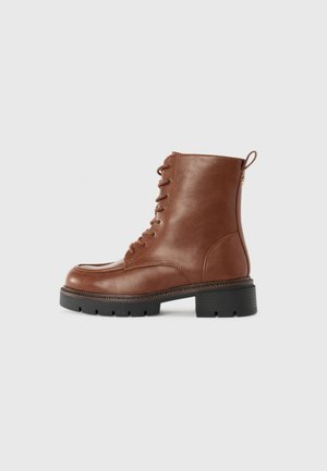 Bottines en cuir marron à lacets avec une semelle épaisse à crampons noirs et une languette au talon, présentées de profil sur fond blanc.