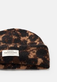 Gehaakte beanie in bruin en zwart luipaardprint. Zachte wolmix. Beschikt over een opgerolde rand met een wit label waarop "MADS NØRGAARD COPENHAGEN" staat.