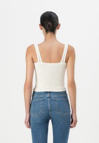 Rutet hvit tanktop med brede stropper, med firkantet hals. Kombinert med tettsittende blå denimjeans som fremhever lommer og sømmer.