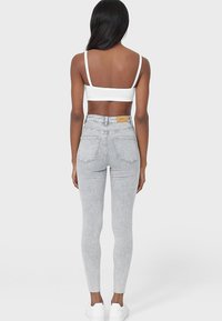 Jeans ajustados de tiro alto en gris con acabado texturizado, bolsillos traseros y una etiqueta de marca en la cintura, combinados con una camiseta corta blanca.