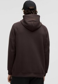 Brauner Kapuzenpullover mit weicher Textur und gerippten Bündchen, der einen lässigen Schnitt und eine glatte Oberflächenbeschaffenheit aufweist.