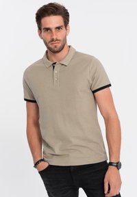 Beige polo triko s černým límečkem a manžetami, s tříknoflíkovou légou a hladkou texturou. Nosit s černými kalhotami.