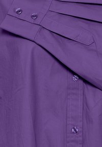 Lila Hemd mit Knöpfen aus leichtem Stoff, das über ein plissiertes Design, metallische Knöpfe und kontrastierende Nähte verfügt.