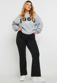 Harmaa huppari, jossa on rohkea musta "1980" ja "PARIS" -painatus, yhdistettynä mustiin leveisiin housuihin. Hupparissa on rento istuvuus ja pehmeä kangas, ja se on yhdistetty valkoisiin lenkkareihin.