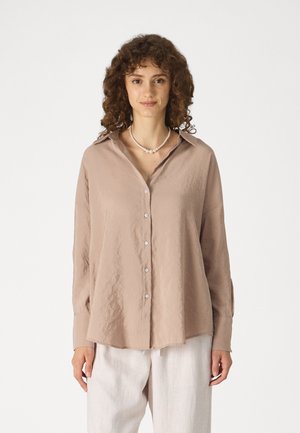 Camisa de manga larga y botones en un suave tejido beige con una textura arrugada. Presenta un collar clásico y un dobladillo recto.