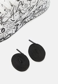 White sneaker featuring black line drawings of flowers and butterflies, accompanied by two black flat shoelaces.