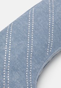 Gros plan d'un tissu en denim bleu clair avec des rangées verticales de petits clous argentés et des coutures visibles le long du bord.