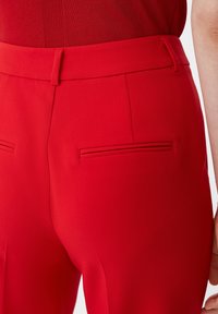 Pantalons ajustés rouges avec une texture lisse, une taille structurée et deux poches plaquées à l'arrière. Le design met en avant une silhouette cintrée.