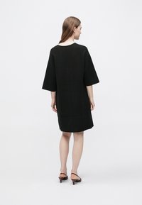 Abito nero oversize con maniche corte e larghe, scollo tondo e silhouette dritta. Tessuto liscio e design minimalista.