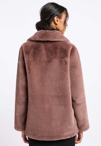 Nepalen jas in stoffige roos, met een brede kraag en een casual pasvorm. De textuur is zacht, met een gladde afwerking en minimale zichtbare stiksels.