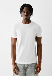 White short-sleeve t-shirt made of cotton with a crew neck, smooth texture, and a fitted design, paired with light grey denim jeans.