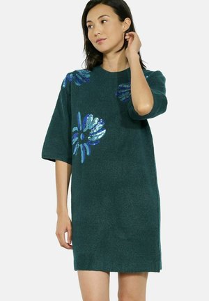 Groene gebreide jurk met korte mouwen, voorzien van blauwe en zilveren bloemsequins op de schouders. Zachte textuur; relaxte pasvorm.